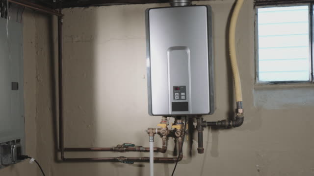 camera moves left from behind a wall to reveal a tankless water heater on the wall in a basement