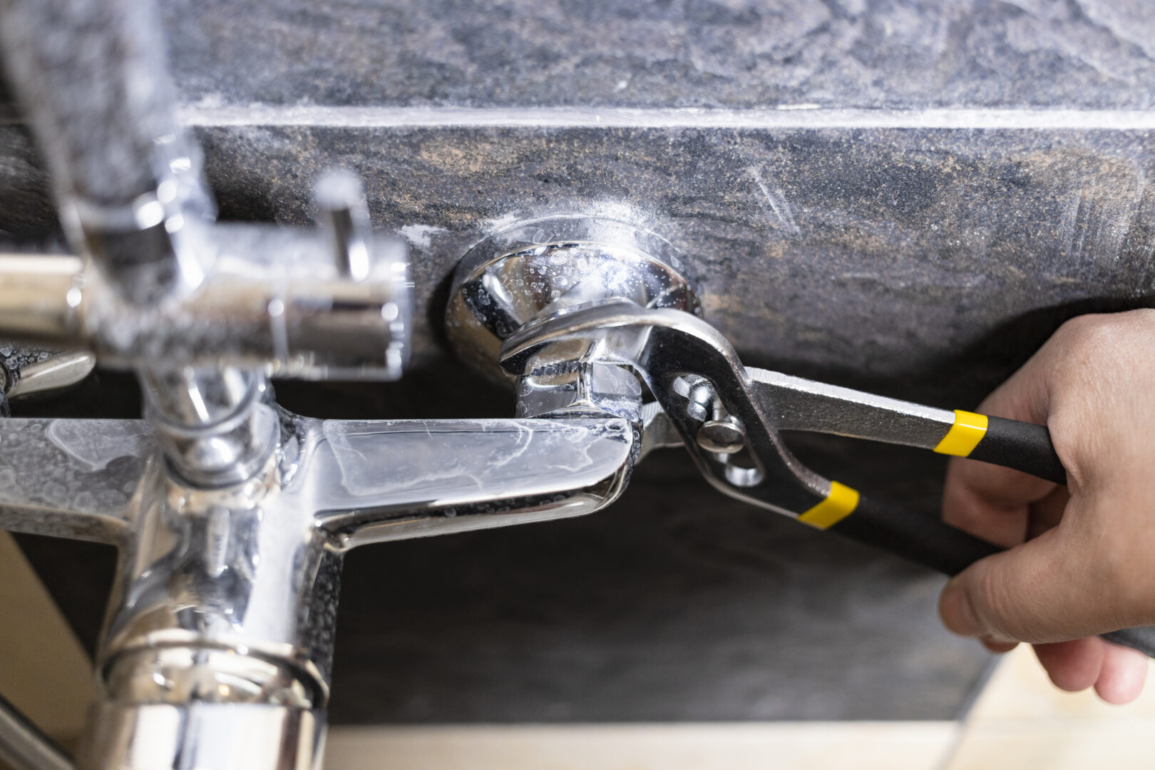 plumber unscrews nut of shower faucet close up on tiled wall at home