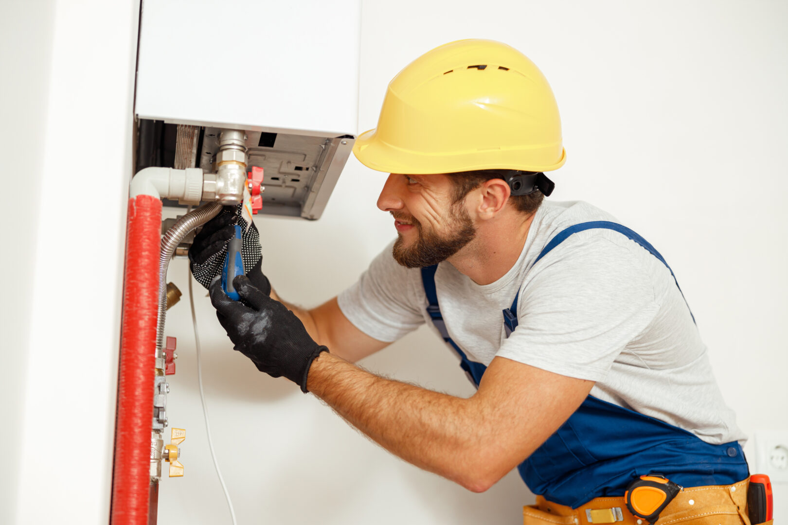 Side view of handyman, technician using screwdriver while fixing boiler or water heater, working on heating system in apartment. Manual work, maintenance, repair service concept